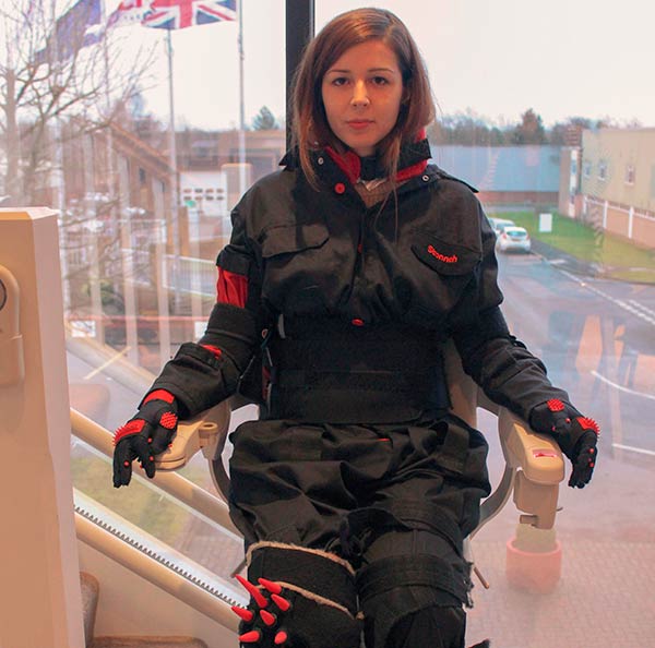 Colaboradora de Stannah con el traje simulador de Artritis, en una silla salvaescaleras